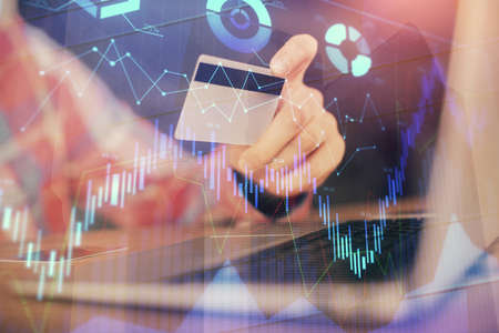 Double exposure of man hands holding a credit card and Forex graph drawing. Stock trading and...