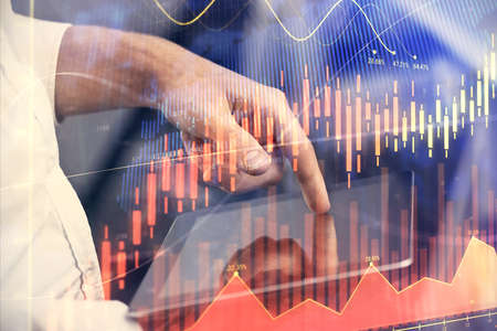 Double exposure of mans hands holding and using a digital device and forex graph drawing. Financial...