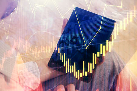Double exposure of mans hands holding and using a digital device and forex graph drawing. Financial...