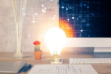 Computer on desktop in office with bulb icon hologram. Double exposure. Concept of idea.