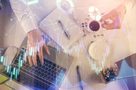 Multi exposure of mans hands typing over computer keyboard and forex graph hologram drawing. Top...