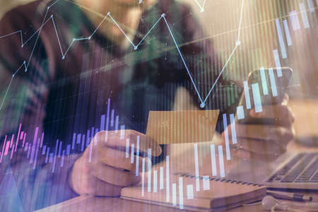 Double exposure of mans hands holding and using a phone and financial graph drawing. Analysis...