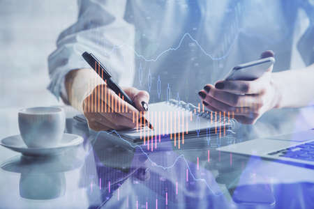 Double exposure of financial graph sketch hologram and woman holding and using a mobile device....