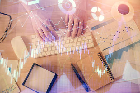 Multi exposure of mans hands typing over computer keyboard and forex graph hologram drawing. Top...