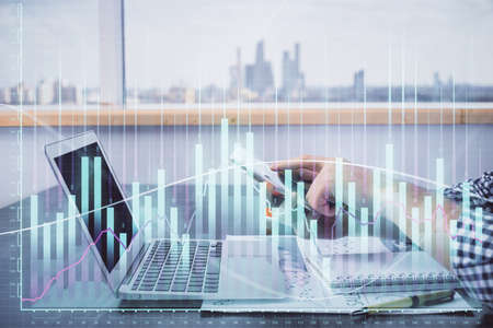 Double exposure of mans hands holding and using a digital device and forex graph drawing. Financial...