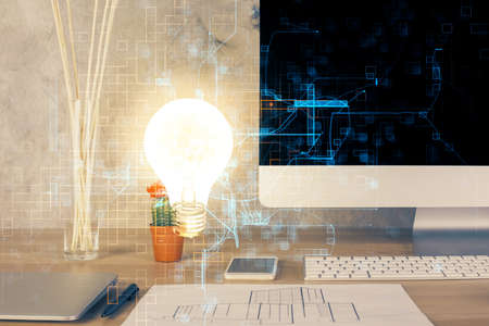 Computer on desktop in office with bulb icon hologram. Double exposure. Concept of idea.