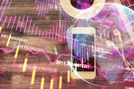 Double exposure of forex chart hologram over desktop with phone. Top view. Mobile trade platform...