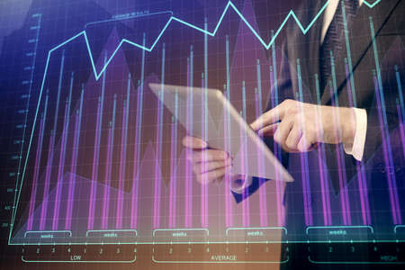 Double exposure of mans hands holding and using a digital device and forex graph drawing. Financial...
