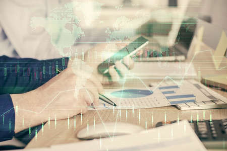 Double exposure of mans hands holding and using a digital device and forex graph drawing. Financial...