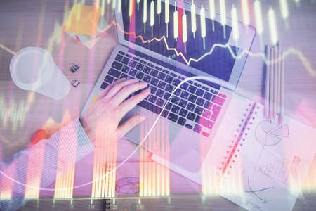 Double exposure of mans hands typing over computer keyboard and forex graph hologram drawing. Top...