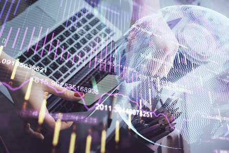 Double exposure of businesswoman hands typing on computer and financial graph hologram drawing....