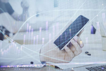 Double exposure of mans hands holding and using a digital device and forex graph drawing. Financial...