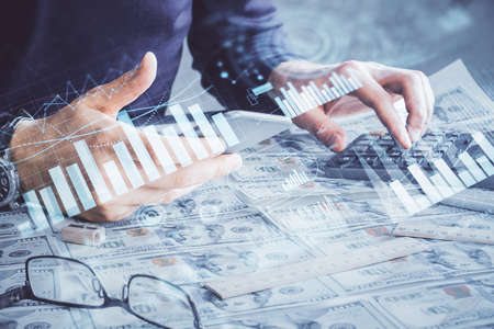 Double exposure of mans hands holding and using a digital device and forex graph drawing. Financial...