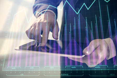 Double exposure of mans hands holding and using a digital device and forex graph drawing. Financial...