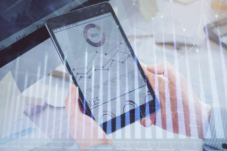 Double exposure of mans hands holding and using a phone and financial graph drawing. Analysis...