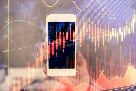 Double exposure of mans hands holding and using a digital device and forex graph drawing. Financial market concept.の写真素材