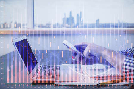 Double exposure of mans hands holding and using a digital device and forex graph drawing. Financial...
