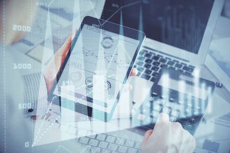 Double exposure of mans hands holding and using a digital device and forex graph drawing. Financial...
