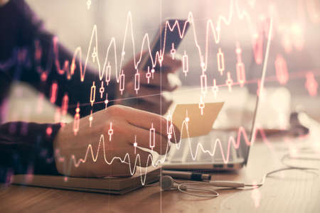 Double exposure of mans hands holding and using a phone and financial graph drawing. Analysis...