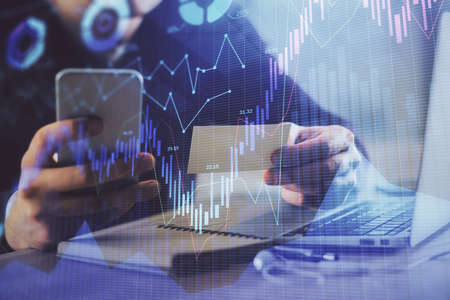 Double exposure of mans hands holding and using a phone and financial graph drawing. Analysis...
