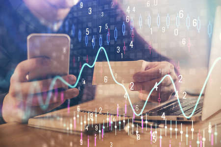 Double exposure of mans hands holding and using a phone and financial graph drawing. Analysis...