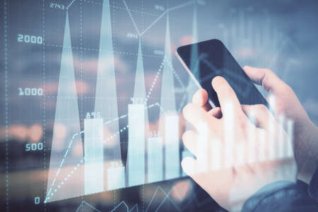 Double exposure of mans hands holding and using a digital device and forex graph drawing. Financial...