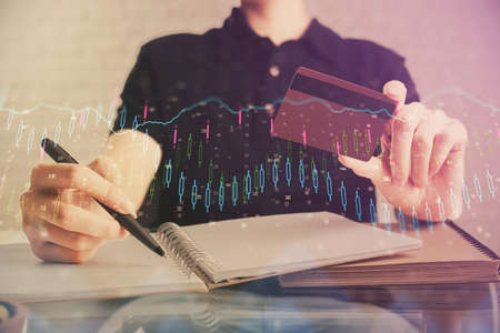 Double exposure of man hands holding a credit card and Forex graph drawing. Stock trading and...