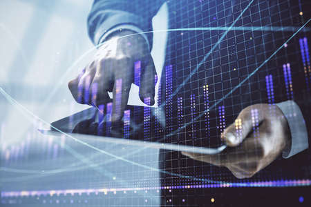 Double exposure of mans hands holding and using a digital device and forex graph drawing. Financial...