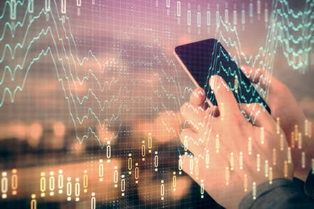 Double exposure of mans hands holding and using a digital device and forex graph drawing. Financial...