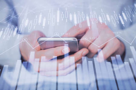 Double exposure of mans hands holding and using a digital device and forex graph drawing. Financial...
