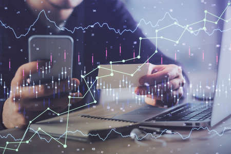 Double exposure of mans hands holding and using a phone and financial graph drawing. Analysis...