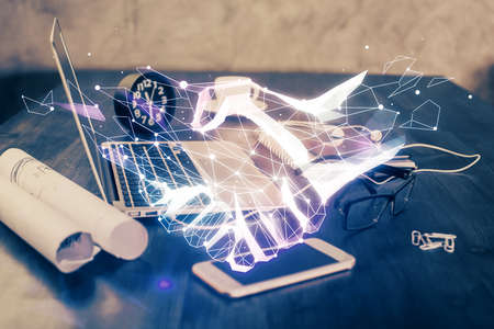 Desktop computer background in office and handshake hologram drawing. Double exposure. Pertnership concept.の写真素材