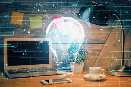 Computer on desktop in office with bulb icon hologram. Double exposure. Concept of idea.