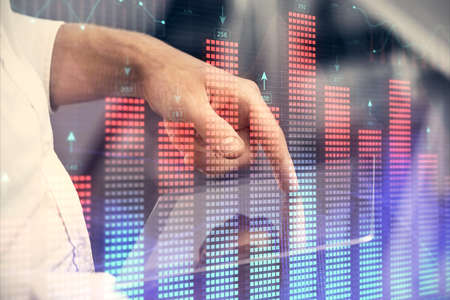 Double exposure of mans hands holding and using a digital device and forex graph drawing. Financial...