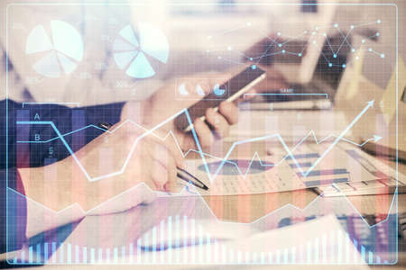 Double exposure of mans hands holding and using a digital device and forex graph drawing. Financial...