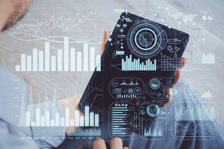 Double exposure of mans hands holding and using a digital device and forex graph drawing. Financial...