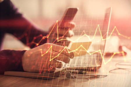 Double exposure of mans hands holding and using a phone and financial graph drawing. Analysis...