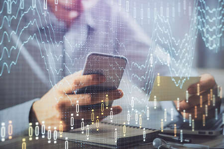 Double exposure of mans hands holding and using a phone and financial graph drawing. Analysis...
