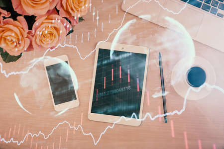 Double exposure of forex graph hologram over desktop with phone. Top view. Mobile trade platform...