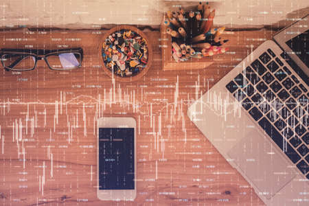 Double exposure of financial graph hologram over desktop with phone. Top view. Mobile trade platform...