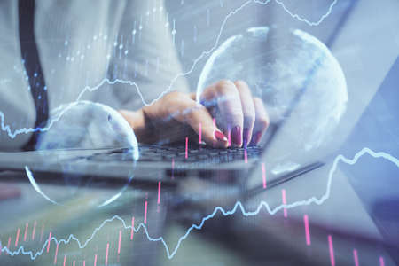 Double exposure of businesswoman hands typing on computer and financial graph hologram drawing....