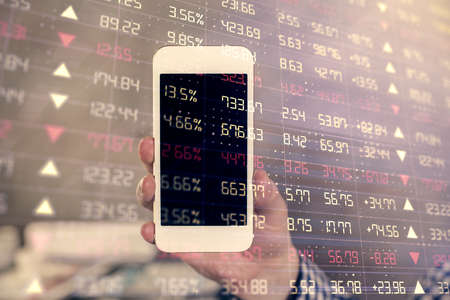 Double exposure of mans hands holding and using a digital device and forex graph drawing. Financial...