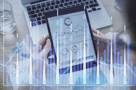 Double exposure of mans hands holding and using a digital device and forex graph drawing. Financial...