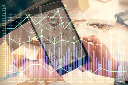 Double exposure of mans hands holding and using a phone and financial graph drawing. Analysis...
