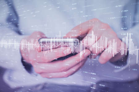 Double exposure of mans hands holding and using a digital device and forex graph drawing. Financial...