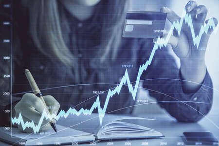 Double exposure of woman on-line shopping holding a credit card and financial graph drawing. Stock market E-commerce concept.の写真素材