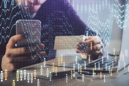 Double exposure of mans hands holding and using a phone and financial graph drawing. Analysis...