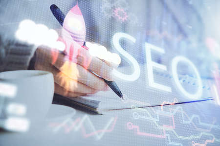 Multi exposure of womans hands making notes with SEO icon. Concept of Search engine optimizationの写真素材