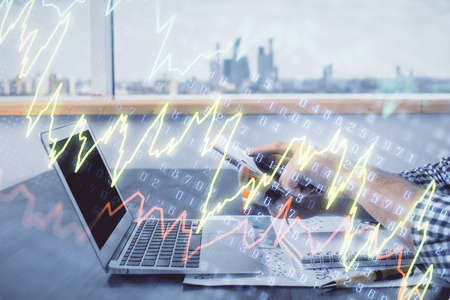 Double exposure of mans hands holding and using a digital device and forex graph drawing. Financial...