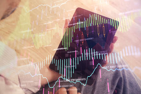 Double exposure of mans hands holding and using a digital device and forex graph drawing. Financial...
